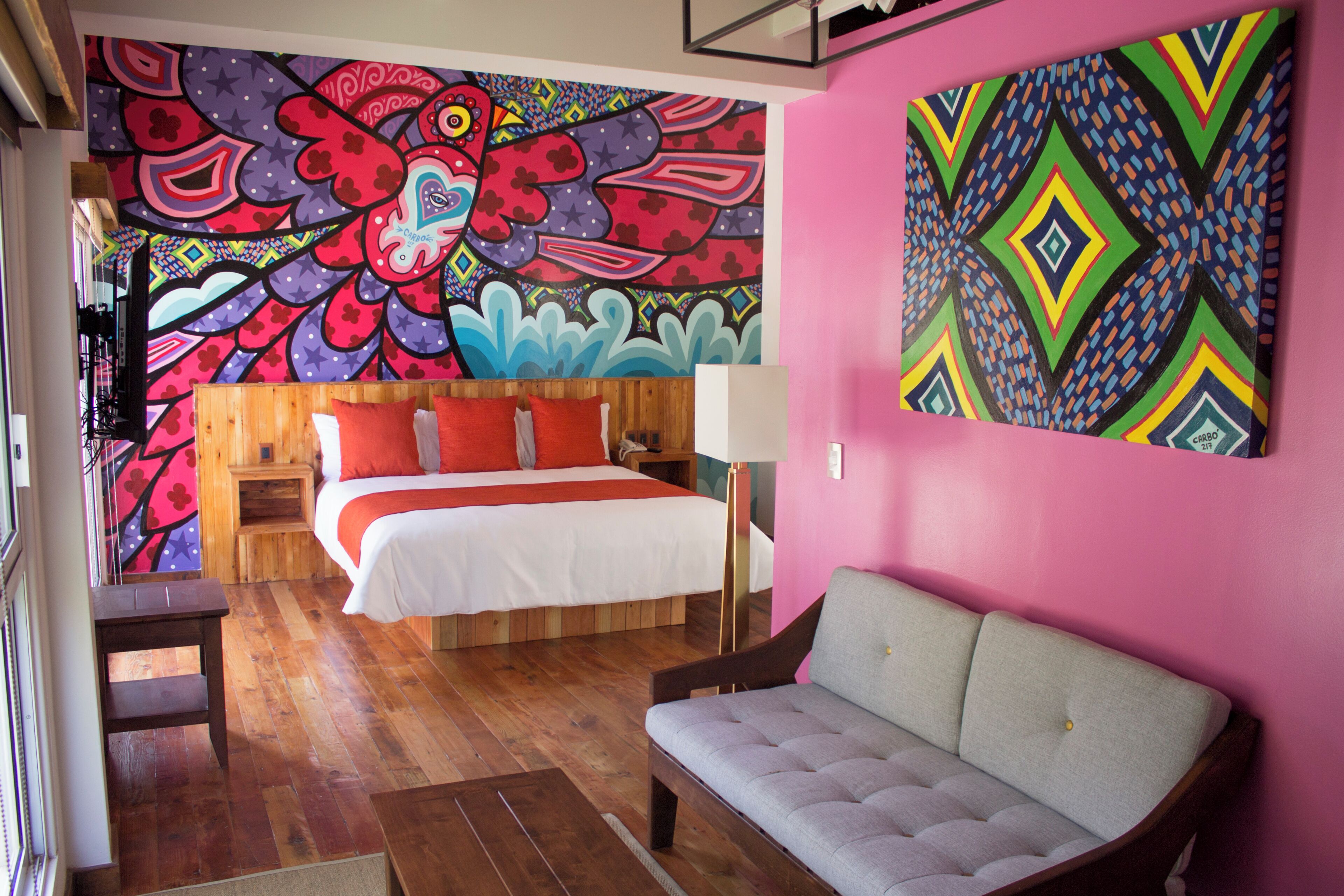 A room with a bed, a sofa, a wall mural, and a wooden floor.