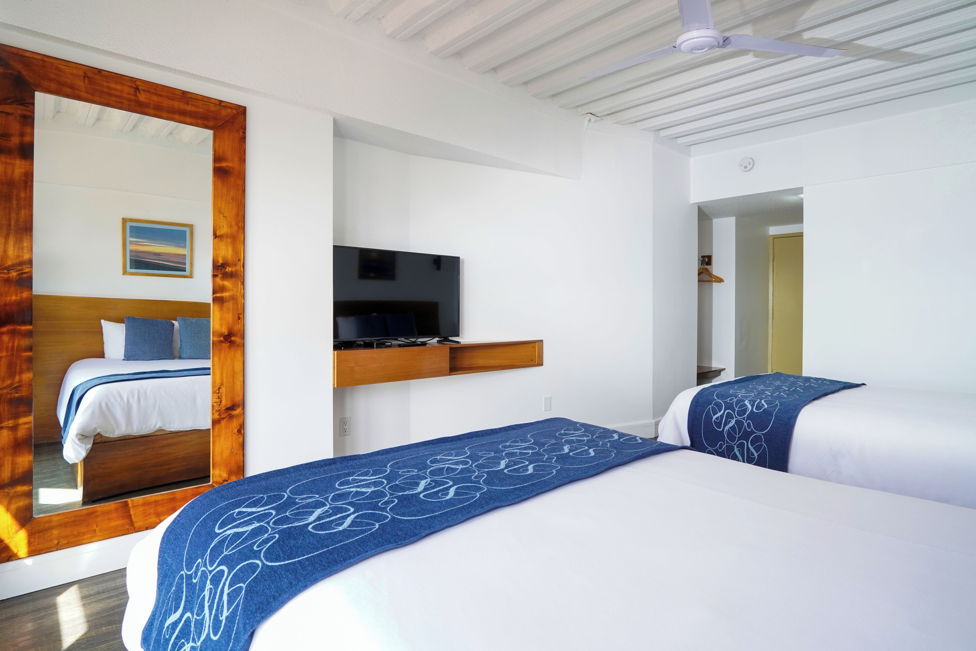Una habitación de hotel con cama, televisión, espejo y cabecera de madera.