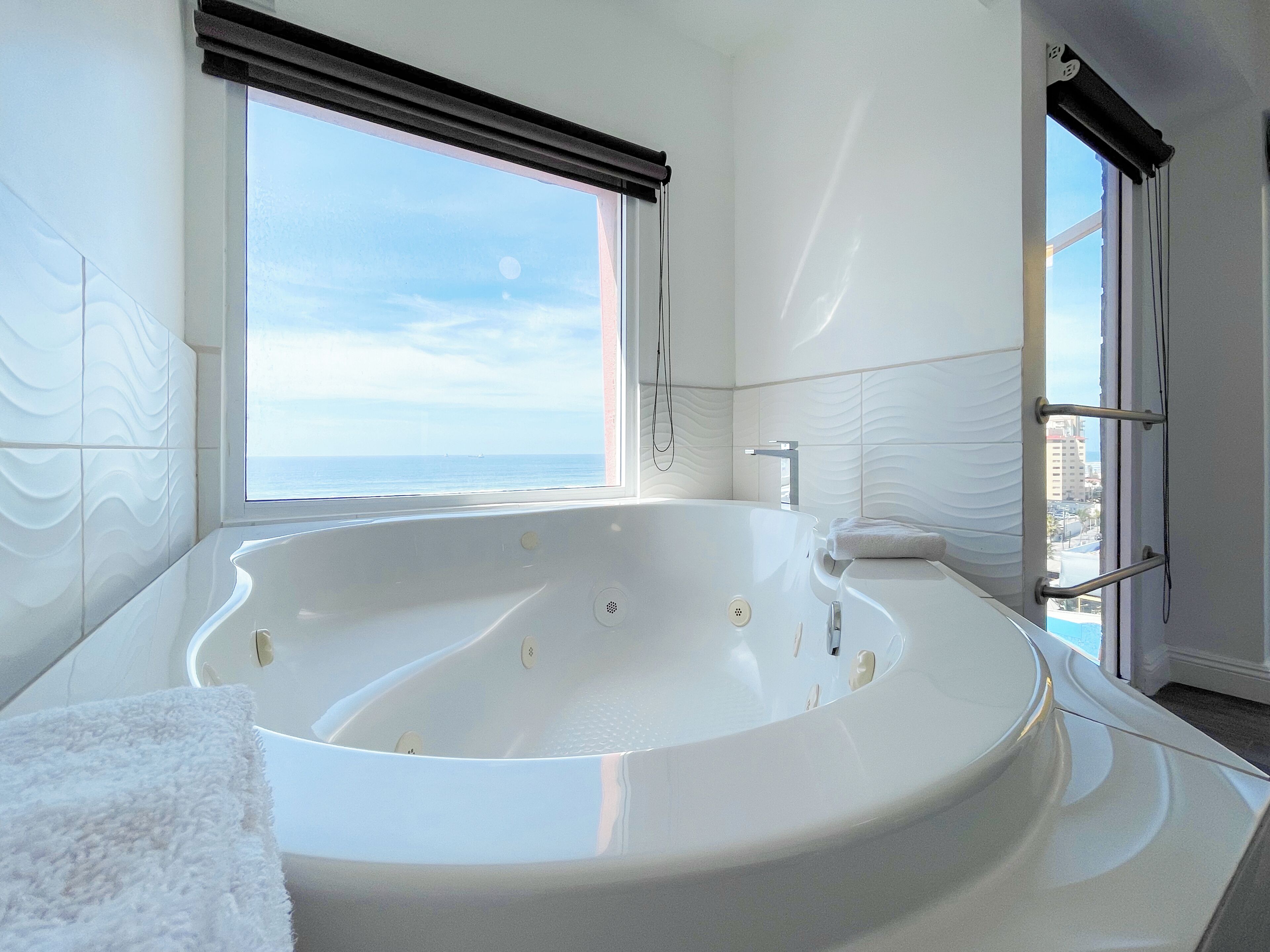 A modern bathroom with a freestanding bathtub, a towel, and a window with a view of the sea.