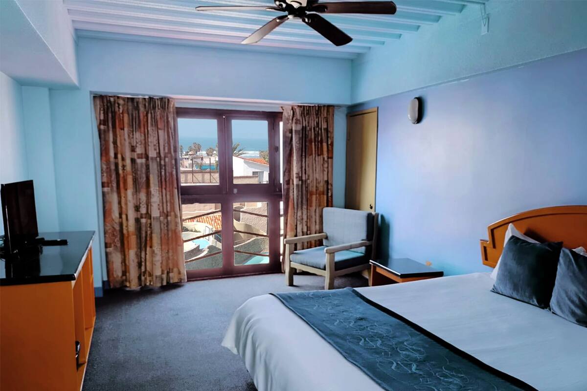 Habitación de hotel con cama, sillón, escritorio y vistas al exterior.