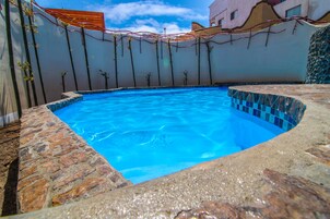 Una piscina con agua azul cristalina, rodeada de baldosas de piedra y un borde alicatado.