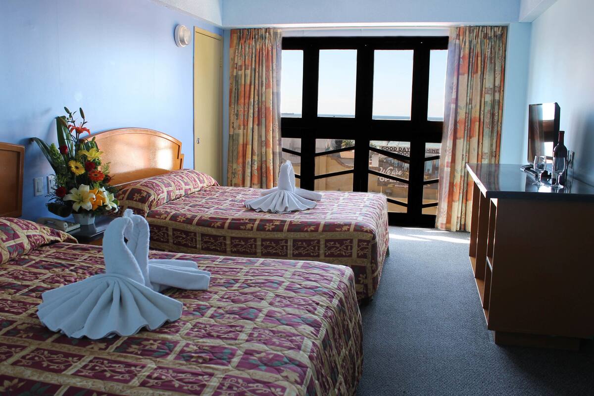 Habitación de hotel con dos camas, un escritorio, una silla, una ventana con cortinas y vistas al exterior.