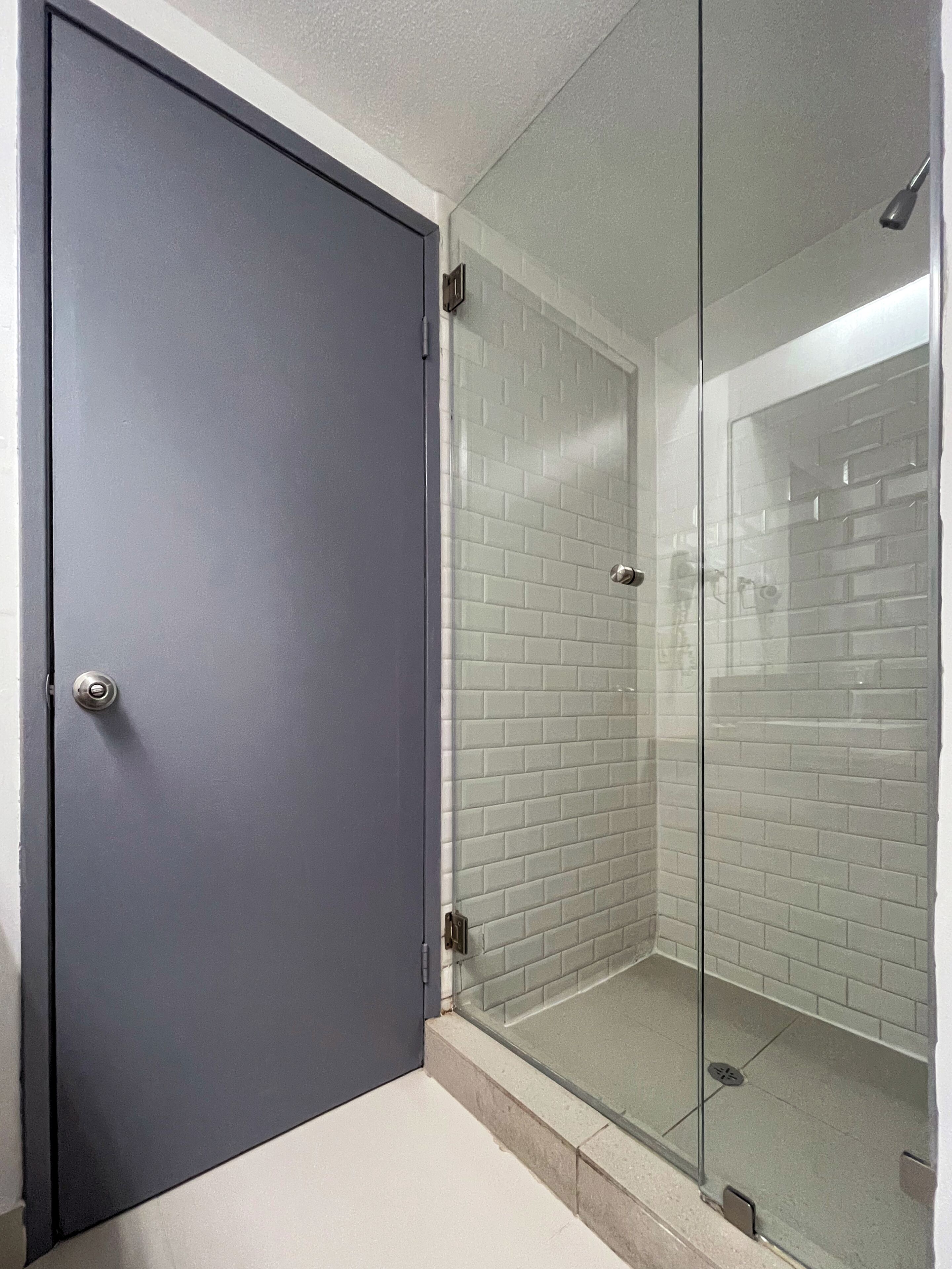 A bathroom with a glass shower enclosure, a white bathtub, and a grey door.