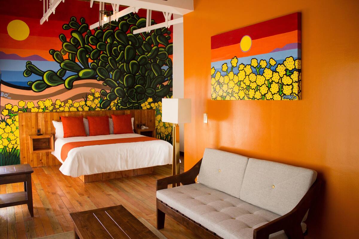 Una habitación con una cama, un sofá, una mesita de noche de madera y un mural en la pared.