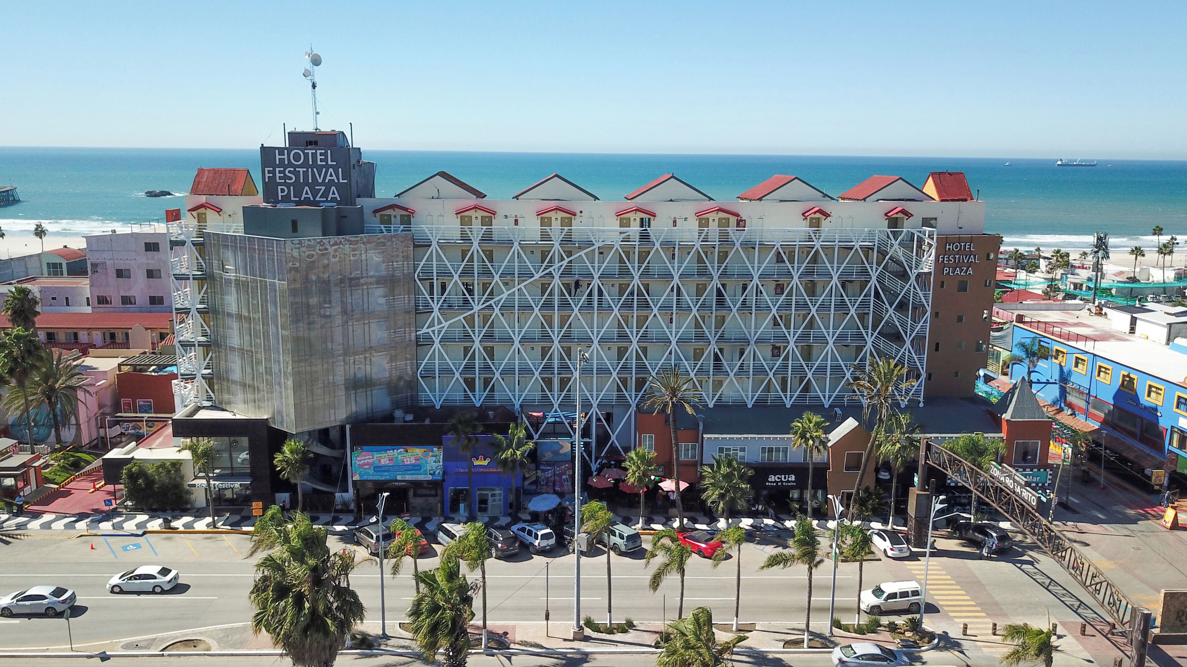 Hotel Festival Plaza, con un diseño arquitectónico moderno, vistas al océano y un estacionamiento con palmeras.