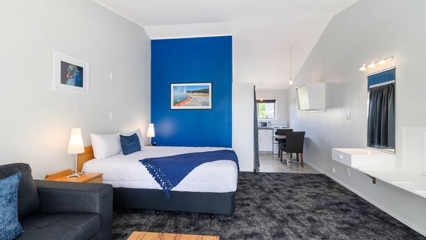 A modern hotel room with a large bed, a desk, a chair, a sofa, a lamp, and a picture on the wall. - Lake Lodge Motel (Rotorua)