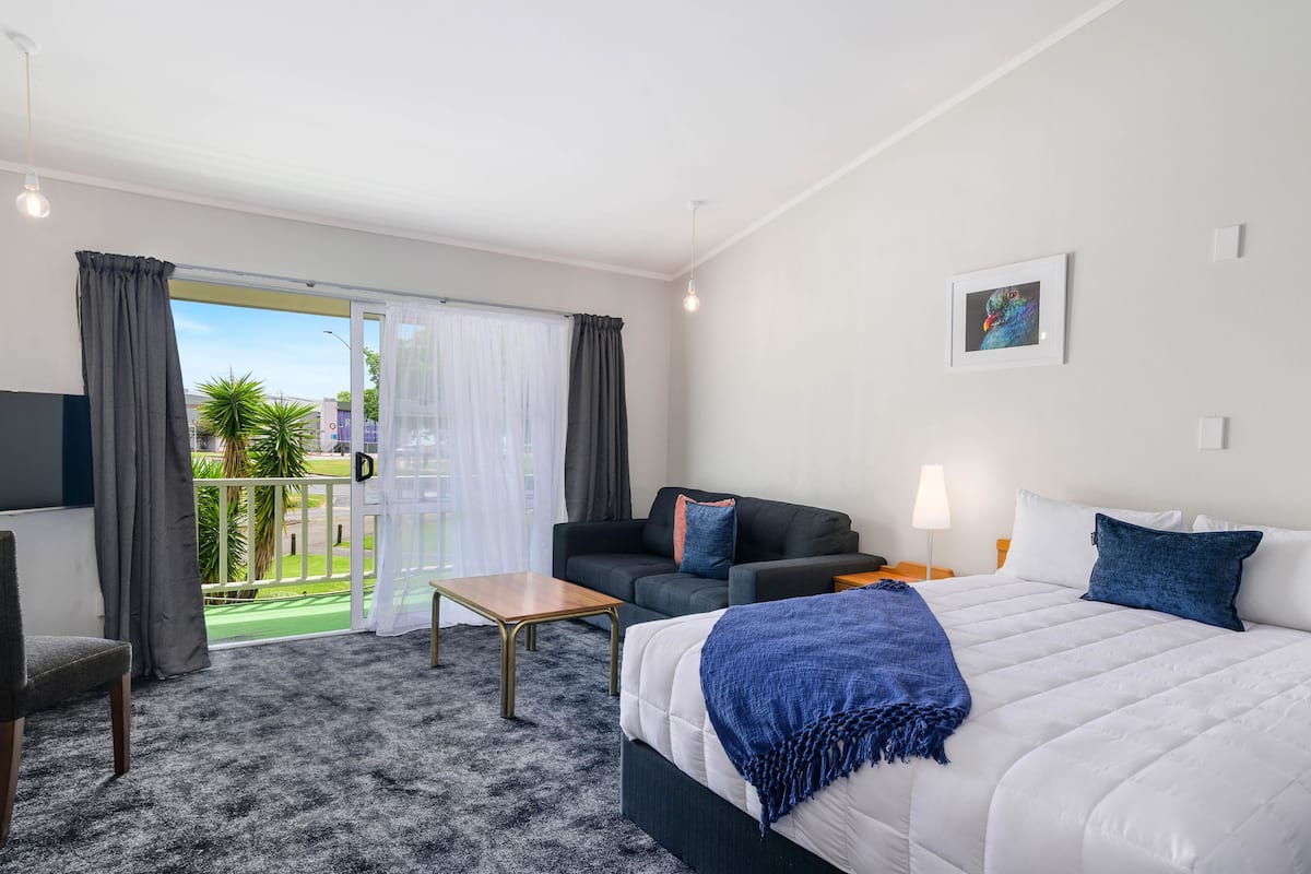 Ein Hotelzimmer mit Bett, Sofa, kleinem Tisch, Lampe und Blick ins Freie.