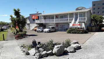 Um motel com área de recepção, várias vagas de estacionamento e um jardim frontal ajardinado com pedras e plantas.