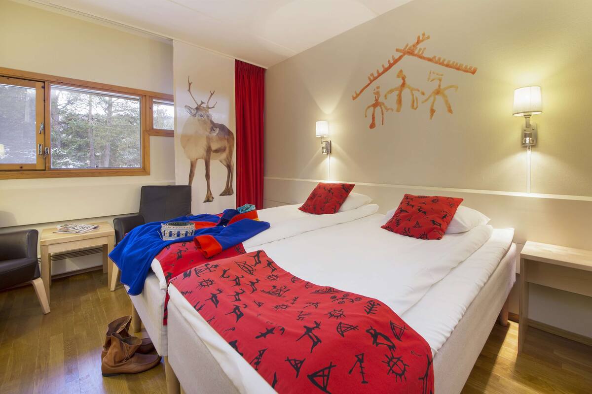 A hotel room with a bed, a desk, a chair, a lamp, and a wall with a deer painting.