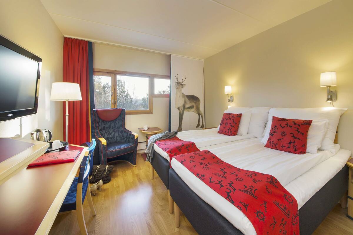 A hotel room with a bed, a desk, a chair, a television, and a window with a view of trees.