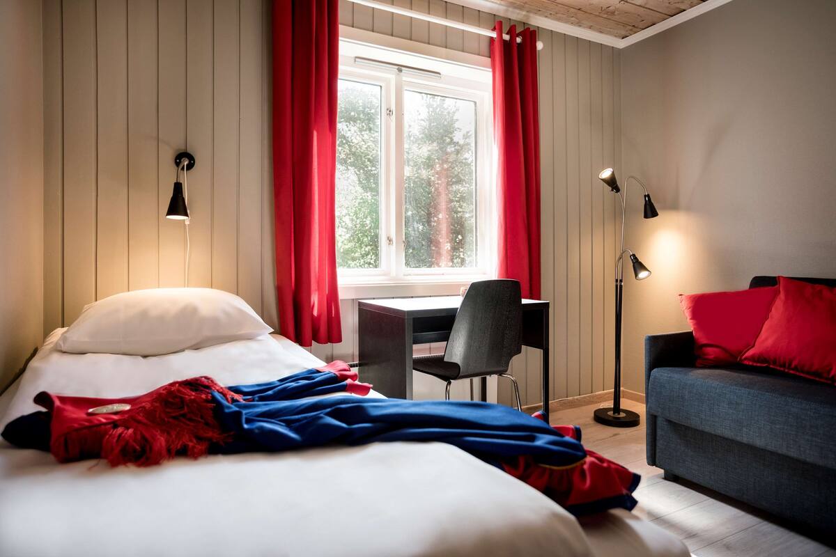 A hotel room with a bed, a desk, a chair, a sofa, and a window with curtains.