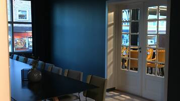 A conference room with a long table and chairs, a vase on the table, and a view through a door to an outdoor seating area.
