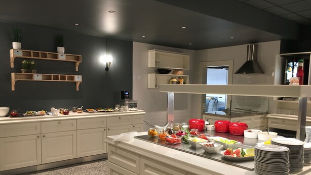 A buffet setup with various food items and utensils, white cabinetry, and a dark wall with shelves.