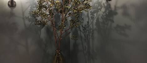 A table with pastries and bread, a vase with branches, and wall-mounted lights against a dark wall.