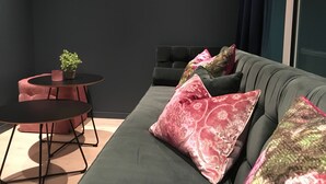 A modern living room with a dark grey sofa, pink patterned pillows, a small round table with a plant, and a dark round coffee table.