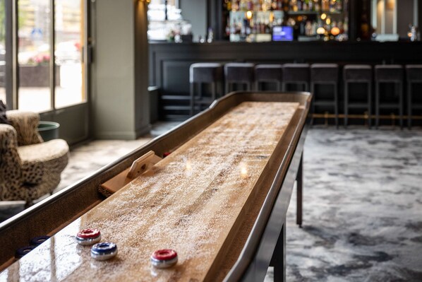 A shuffleboard table in a bar area with a bar and seating in the background. - Quality Hotel Grand Larvik (Larvik)