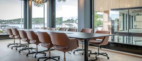 A conference room with a long table and modern chairs, large windows with a view of a cityscape, and a unique chandelier.