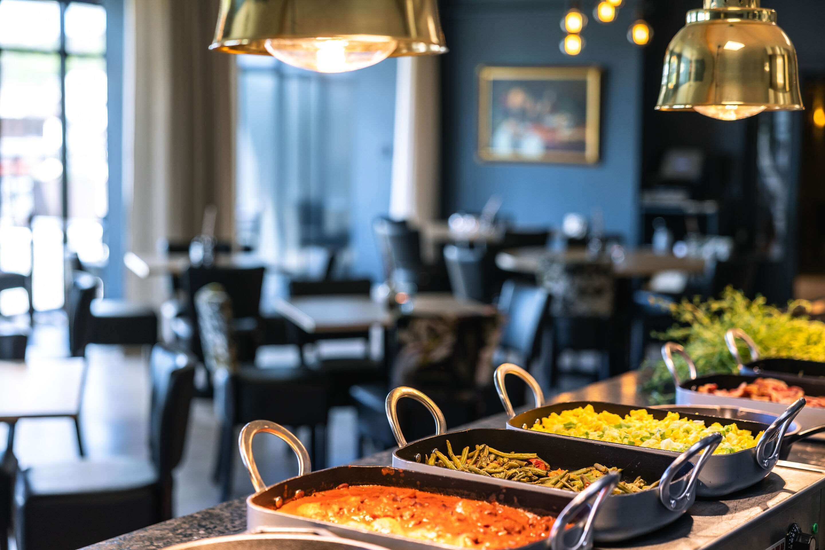 Un buffet proposant divers plats, notamment des pâtes et des légumes, dans un restaurant avec des tables et des chaises.