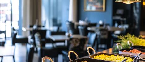 Un buffet proposant divers plats, notamment des pâtes et des légumes, dans un restaurant avec des tables et des chaises.