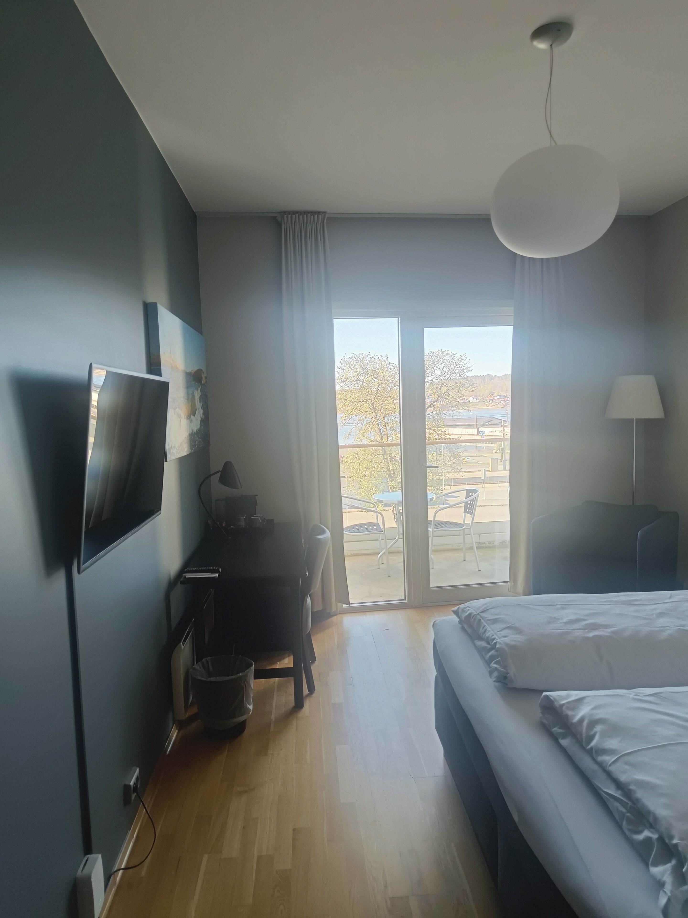 Habitación de hotel con cama, escritorio, televisión, lámpara y vista al exterior.