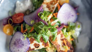 Primer plano de una ensalada con diversas verduras y un trozo de queso a la plancha.