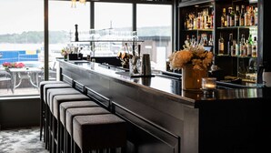 Zona de bar con taburetes, barra y estantería con botellas.
