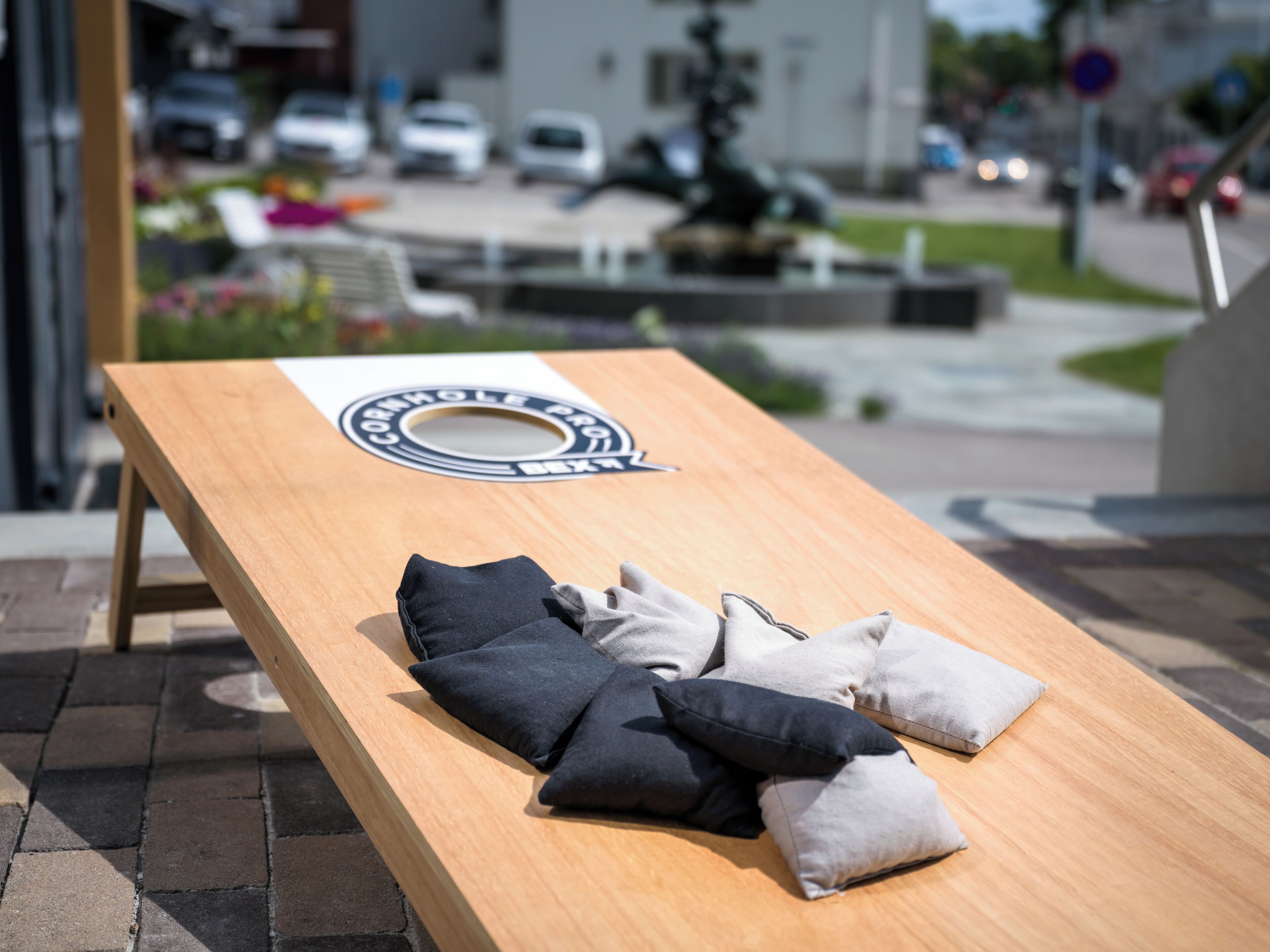 A wooden lounge chair with cushions, a circular logo, and a view of a street with cars and buildings in the background.