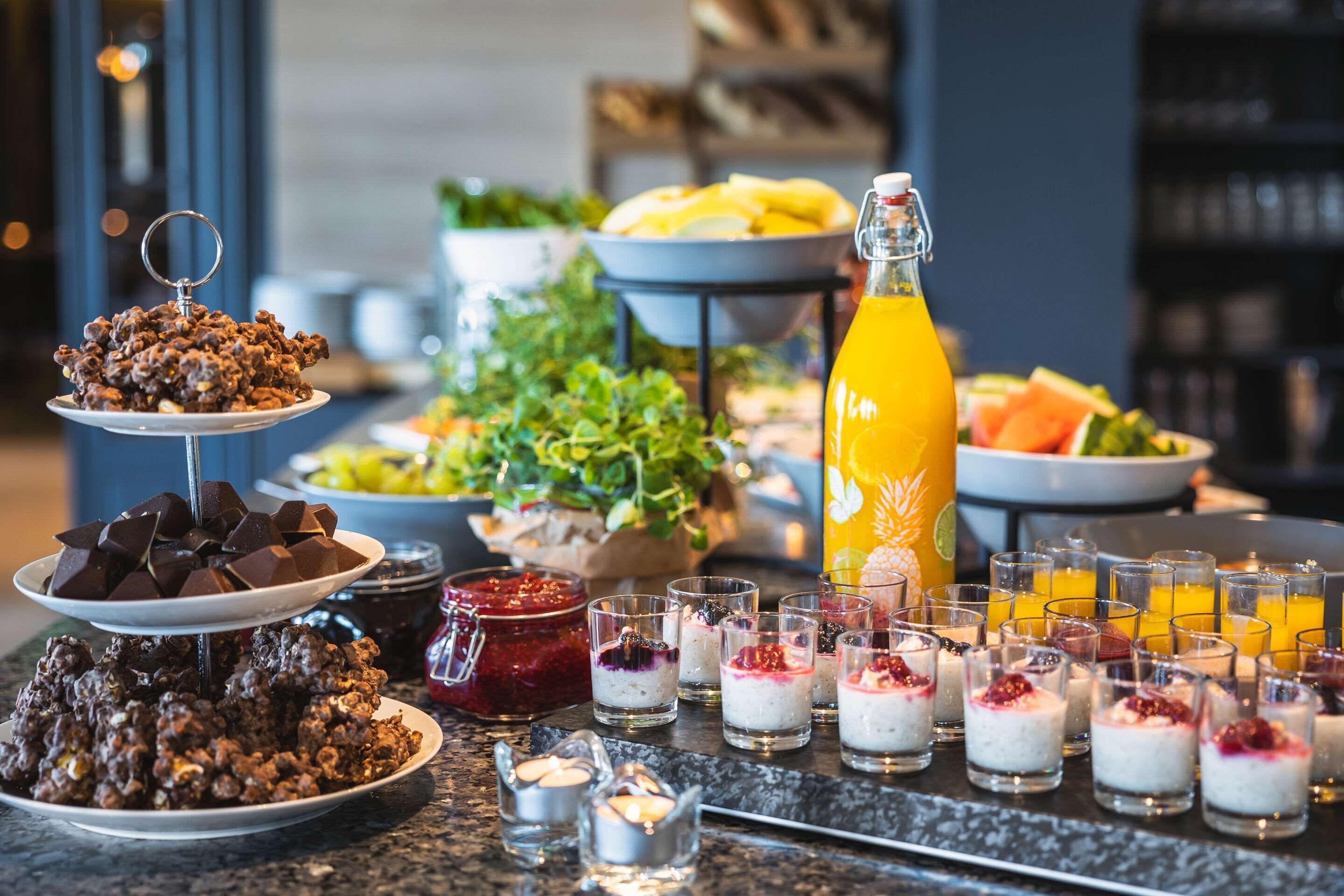 Una mesa de buffet con diversas opciones de comida y bebidas, incluyendo dulces de chocolate, fruta y refrescos.