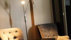 A room with two tufted armchairs and a small table, a floor lamp, and a door with a number sign.