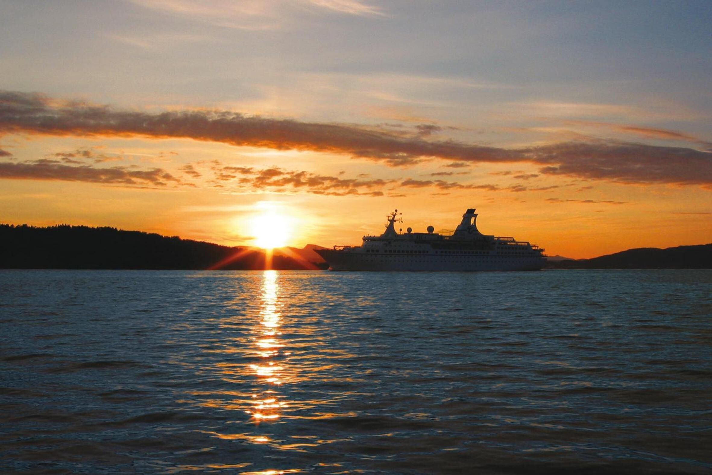 Een cruiseschip bij zonsondergang, met een helder zicht op de boeg en de zon die in het water weerspiegelt.