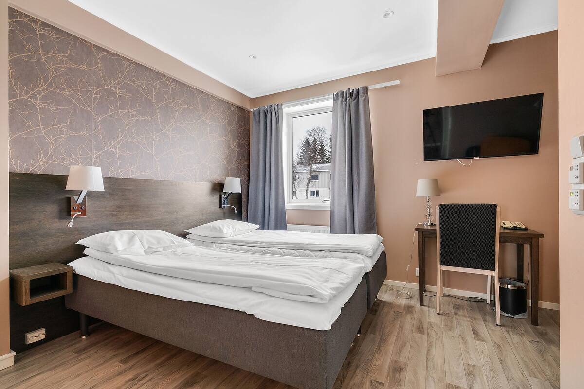 A modern hotel room with a large bed, two bedside tables, a TV, and a view of the outside.