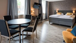 A modern hotel room with a bed, a desk, a round table with chairs, and a TV.