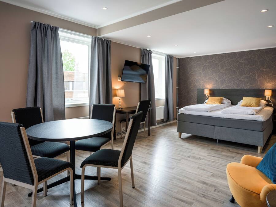 Una habitación de hotel moderna con cama, escritorio, una mesa redonda con sillas y televisor.