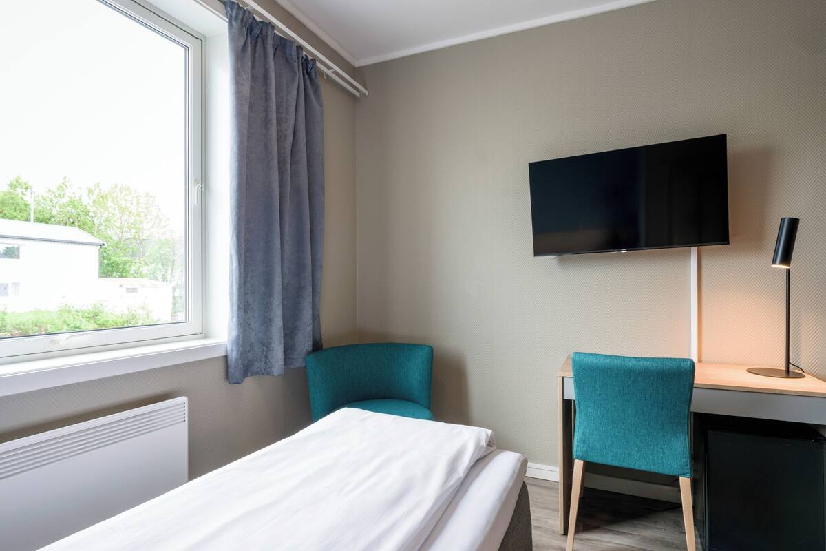A hotel room with a bed, a desk, a chair, a TV, and a window with curtains.
