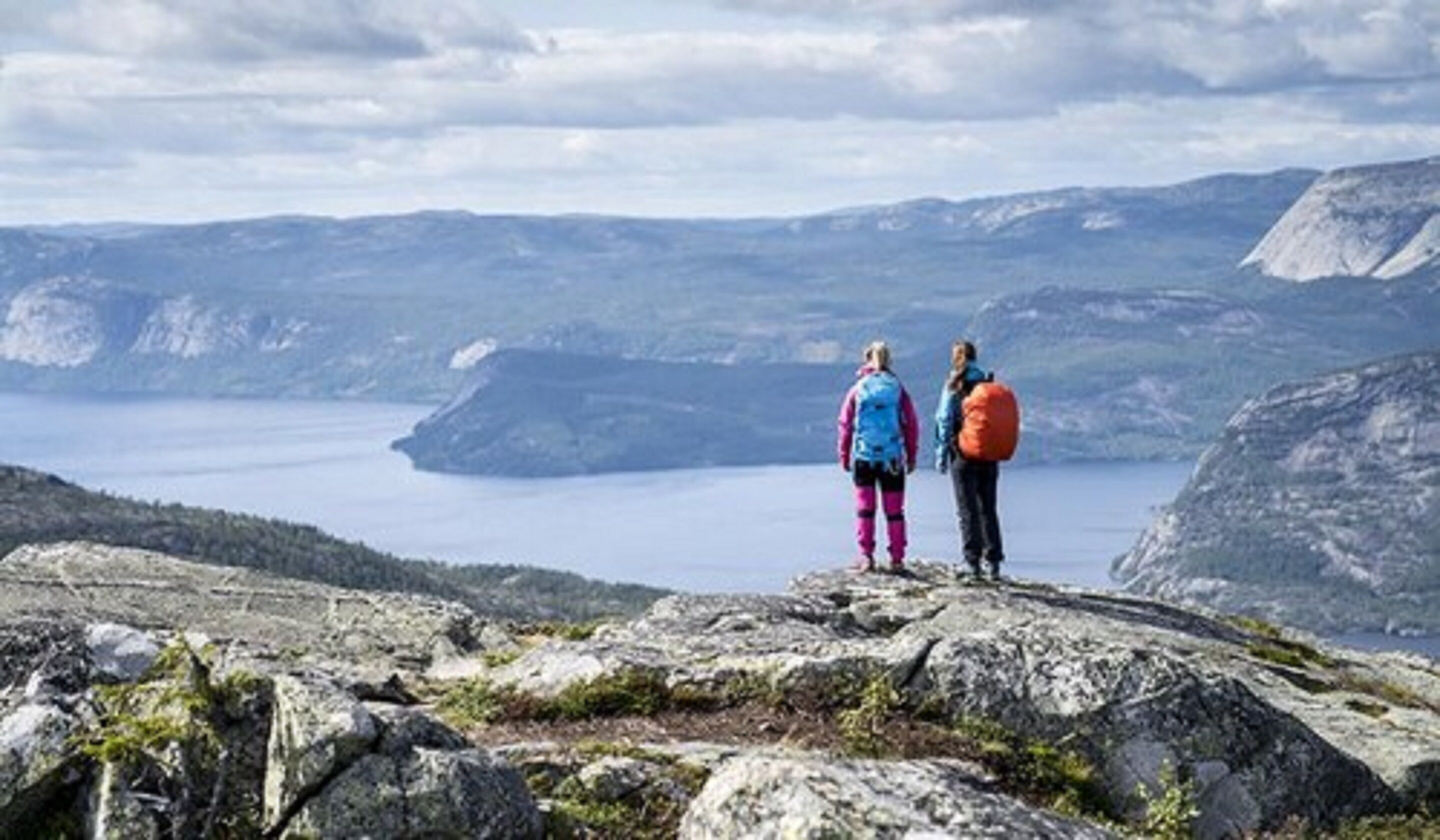 Deux personnes se tiennent debout sur un promontoire rocheux, d’où elles dominent un lac et des montagnes.