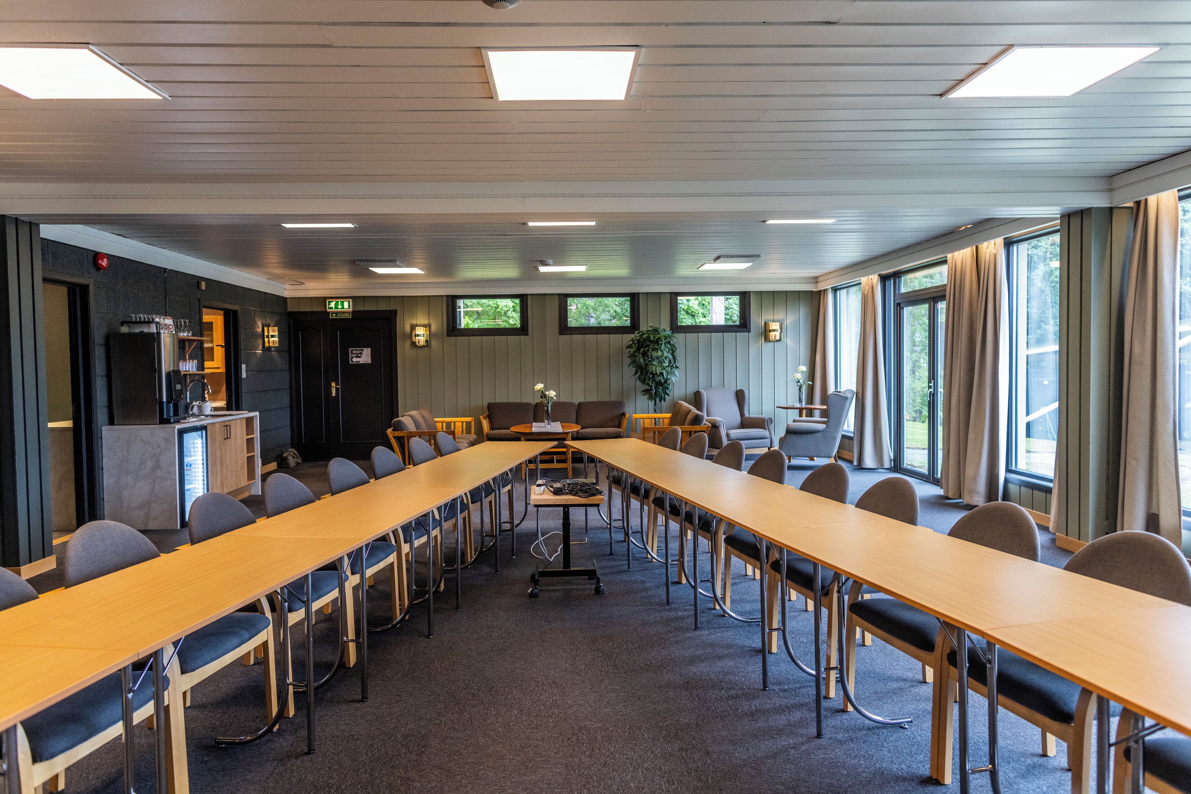 A conference room with a long table, chairs, a small kitchenette, and large windows.