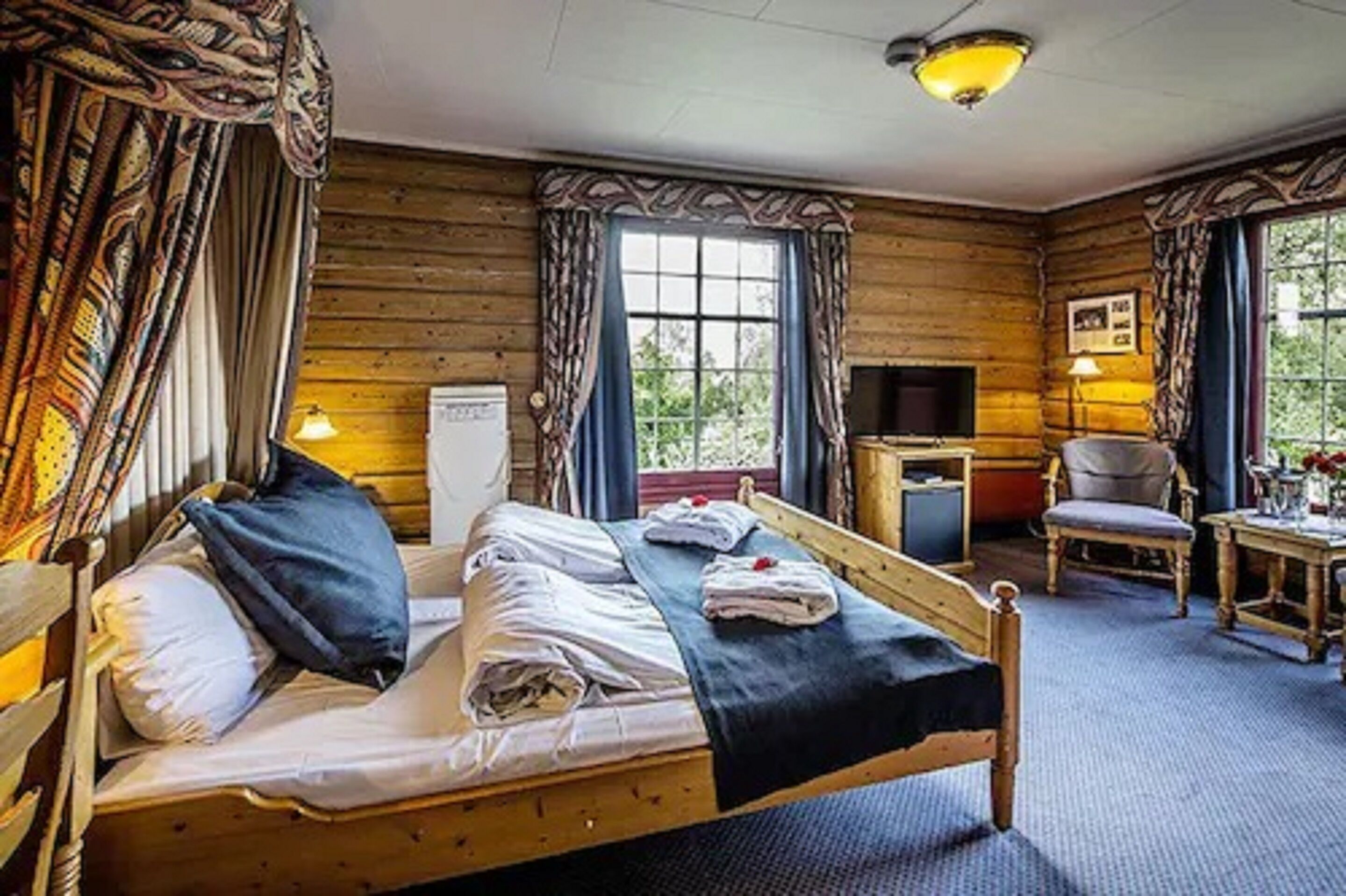 Una habitación tipo cabaña de madera con una cama, un escritorio, una silla y un televisor.