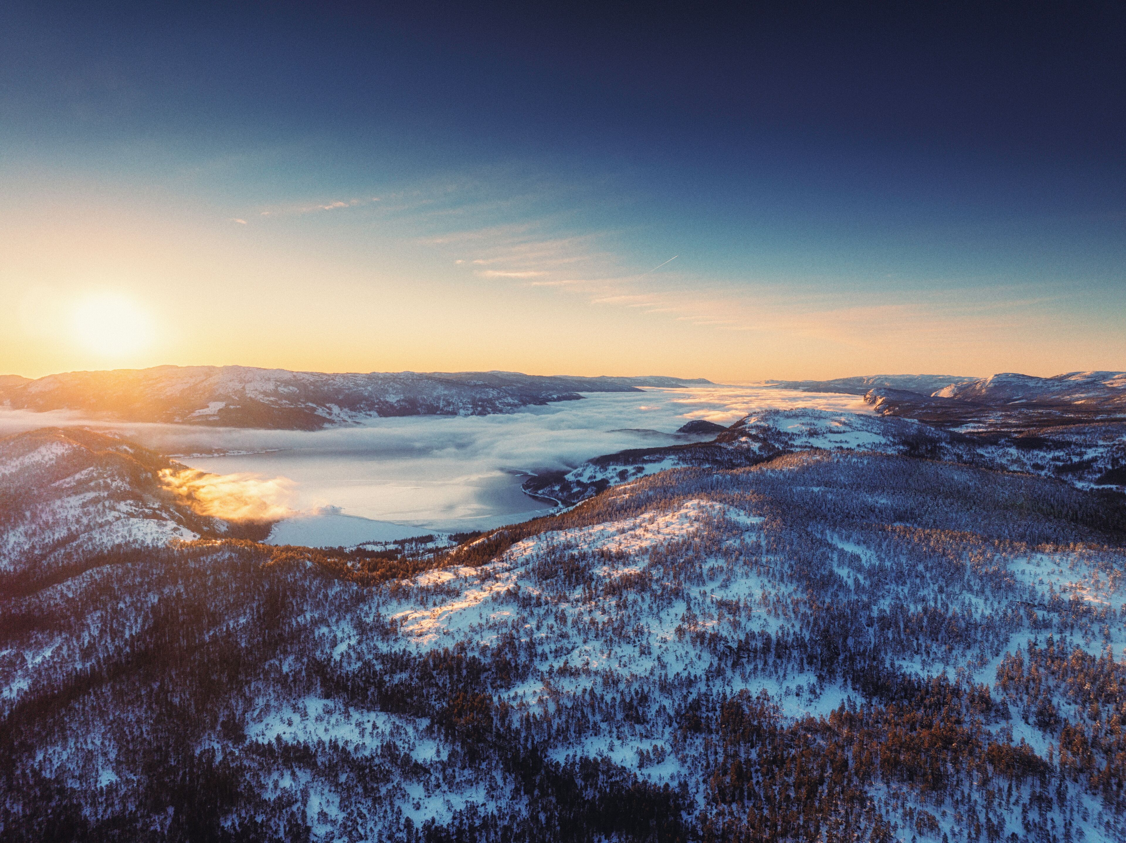 A panoramic view of a mountainous landscape with snow-covered forests and a lake at sunrise.