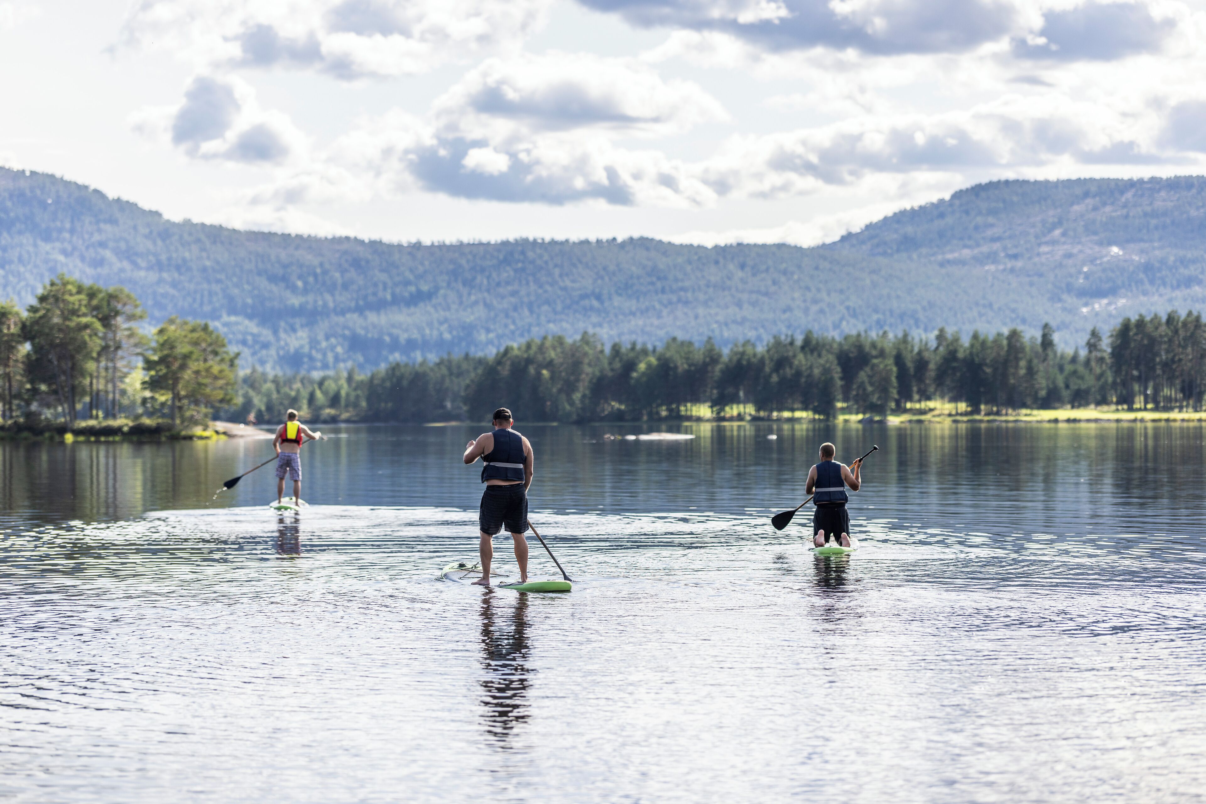 Two people paddleboarding on a calm lake with mountains in the background.