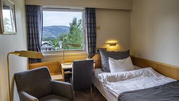 A hotel room with a bed, two armchairs, a desk, and a window with curtains.