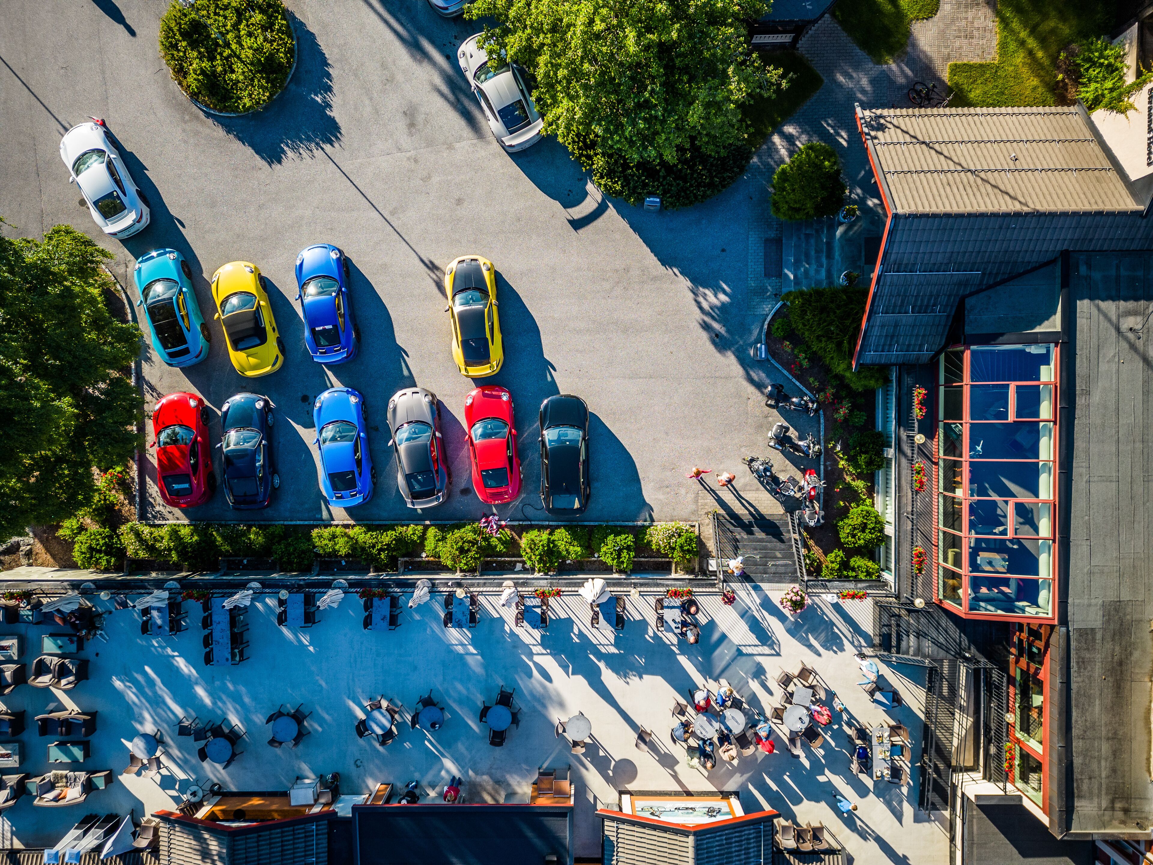 Vista aerea di un parcheggio con diverse auto e un edificio con facciata rossa.
