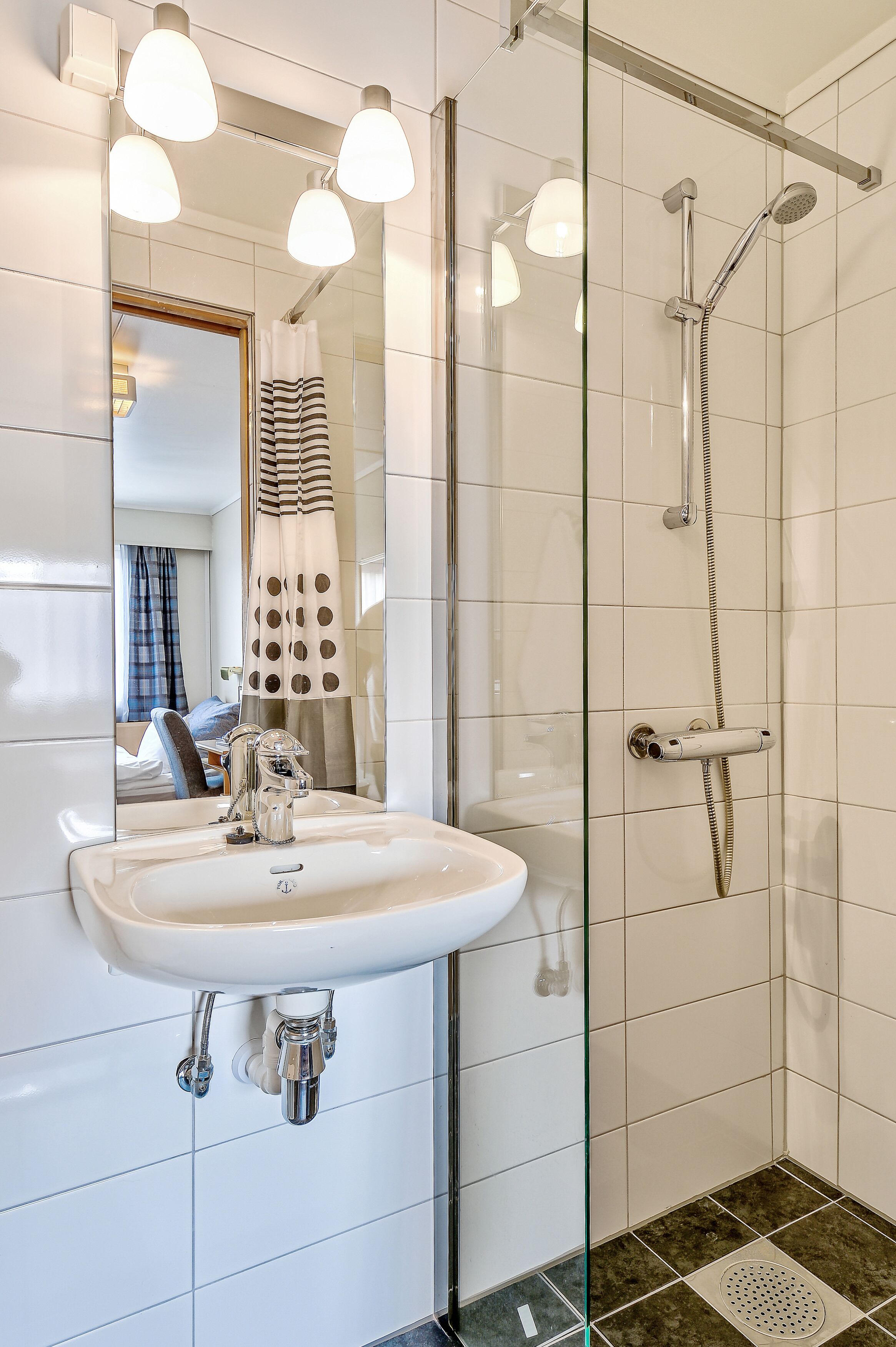 A modern bathroom with a glass shower enclosure, a white sink, and a mirror with lights.