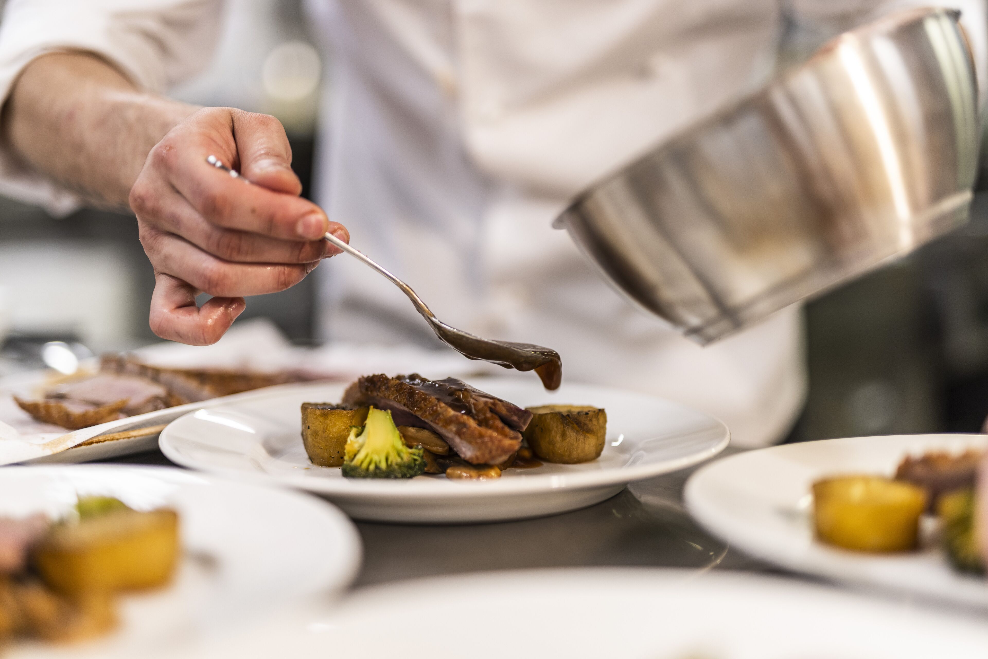 A person pouring sauce over food on a plate.