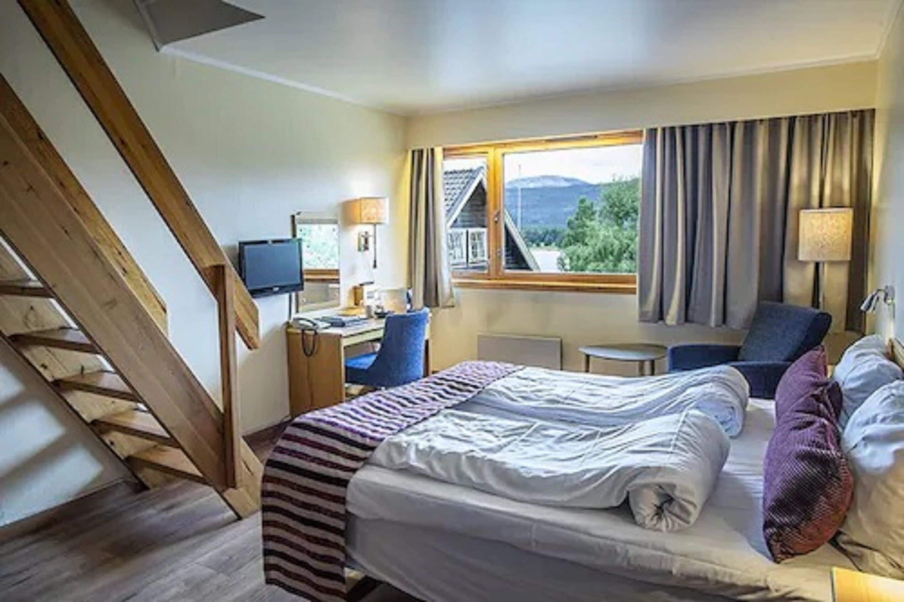 A hotel room with a bed, a desk, a chair, a television, and a window with curtains.