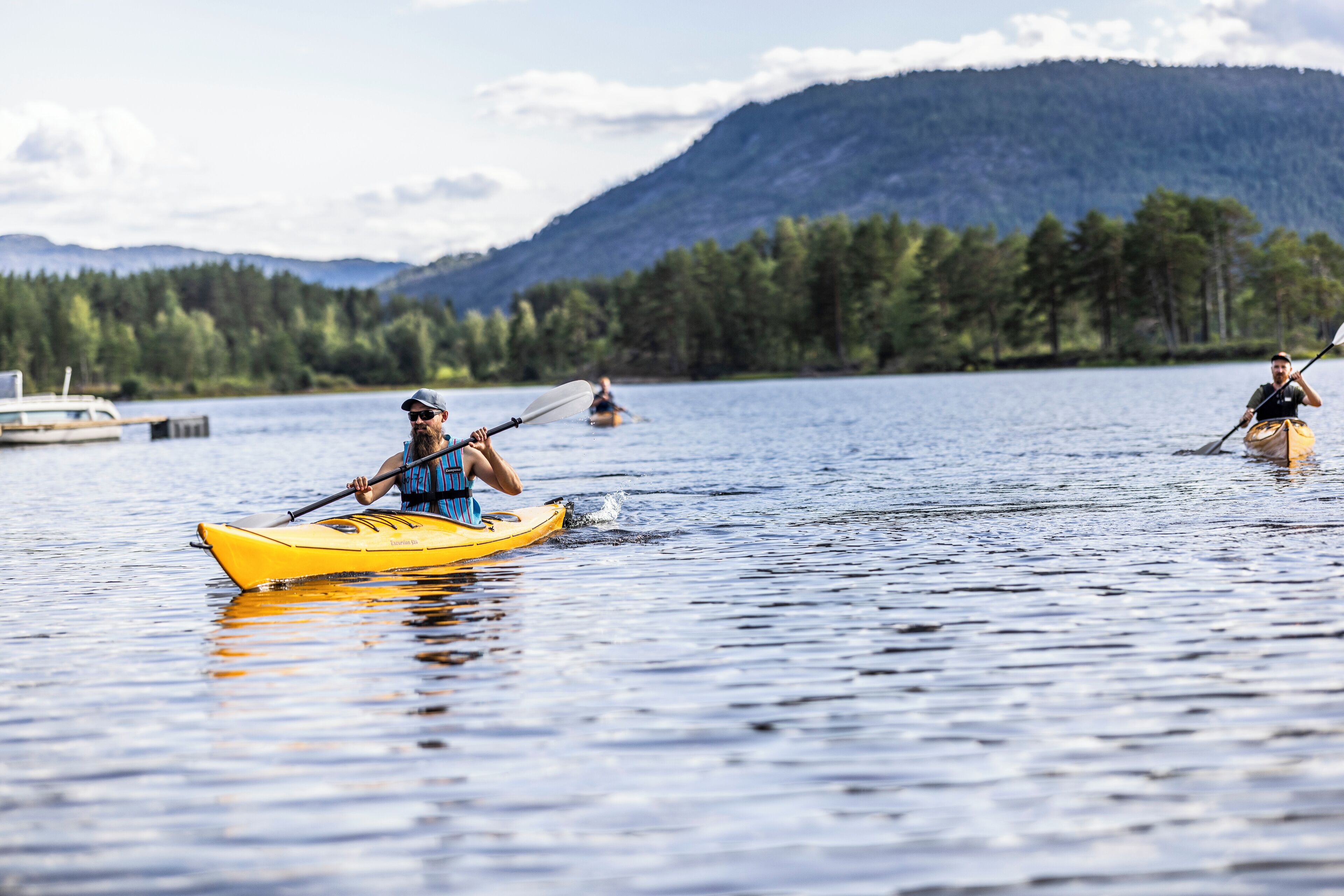 A calm lake with kayakers in yellow and black kayaks.