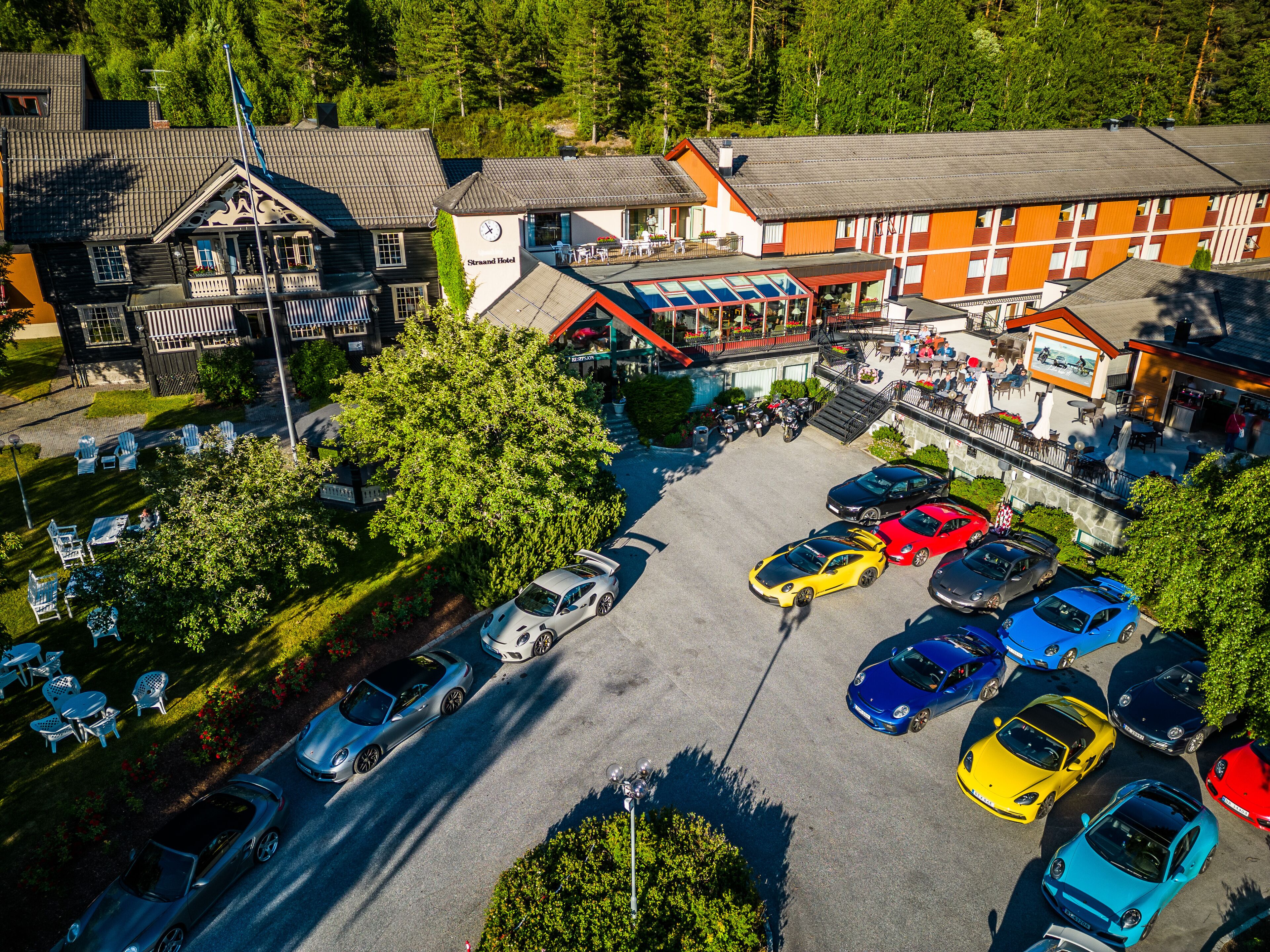 A hotel with a parking lot filled with cars, surrounded by greenery and buildings.