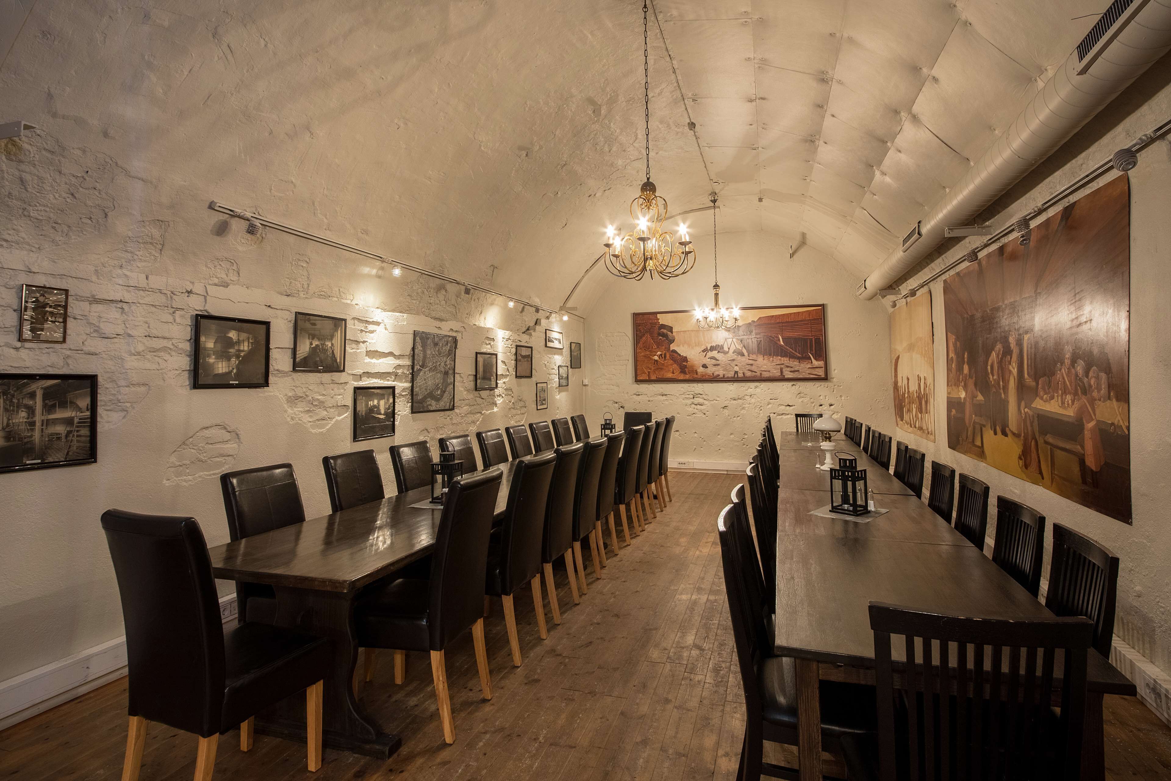 Uma longa mesa de jantar com cadeiras, um candelabro e quadros nas paredes.