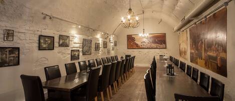 Uma longa mesa de jantar com cadeiras, um candelabro e quadros nas paredes.