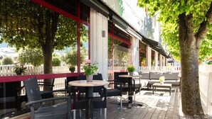 Un patio al aire libre con sillas y mesas de mimbre, una terraza de madera y plantas en macetas.