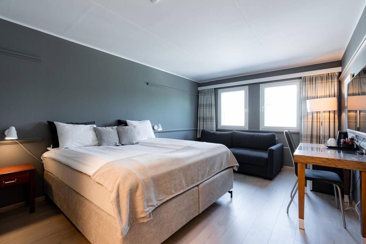 Una habitación de hotel moderna con una cama grande, un sofá, una mesa de comedor y un escritorio.